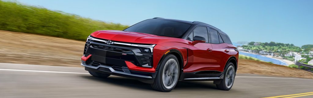 Red Chevrolet electric SUV driving on a scenic road.