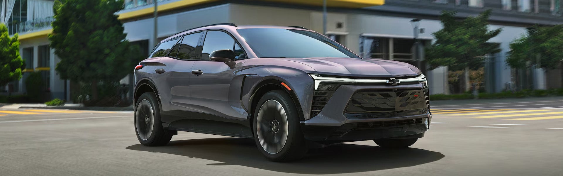 Gray Chevrolet SUV driving through a city street with a modern urban background.