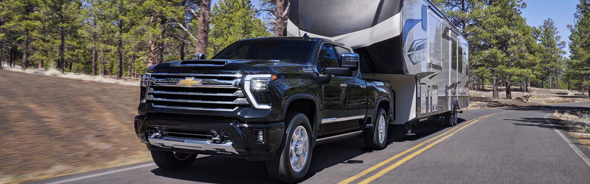 Black Chevrolet Silverado towing a travel trailer on a wooded road.